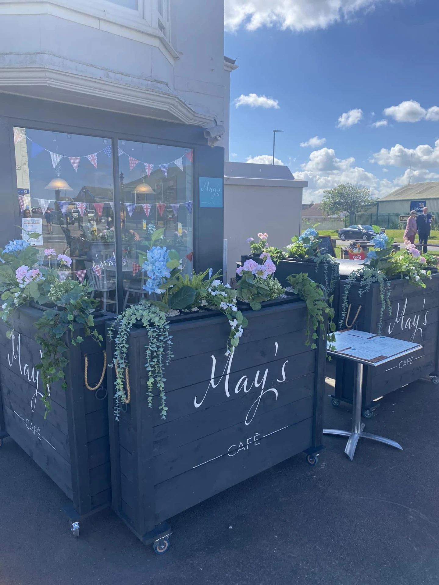 Outside May's Café on a sunny day, with planters full of flowers